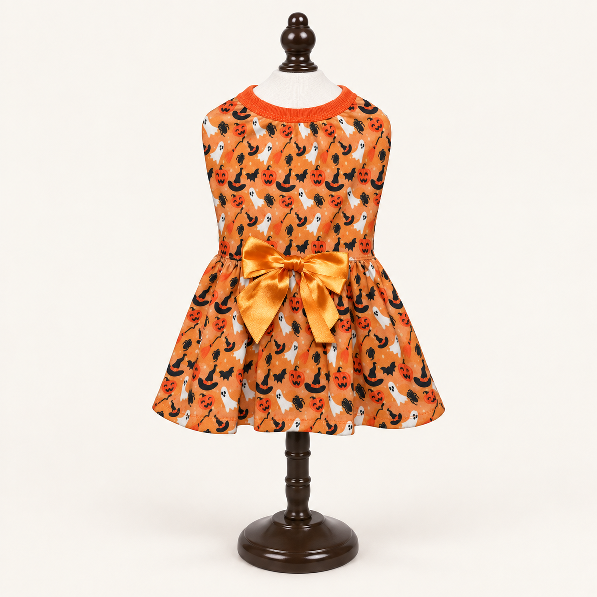Orange Halloween dog dress with a repeating black and white pumpkin print and a large orange satin bow at the waist, displayed on a mannequin stand.