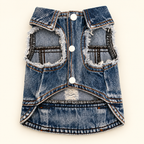 A dog vest made from blue denim jeans, styled with white buttons, frayed edges, and distressed details, laid flat on a light cream background.