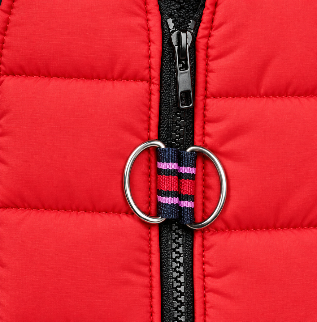 Close-up of a bright red puffer jacket with a black zipper, silver metal O-ring, and a striped web tie in navy, red, and pink.