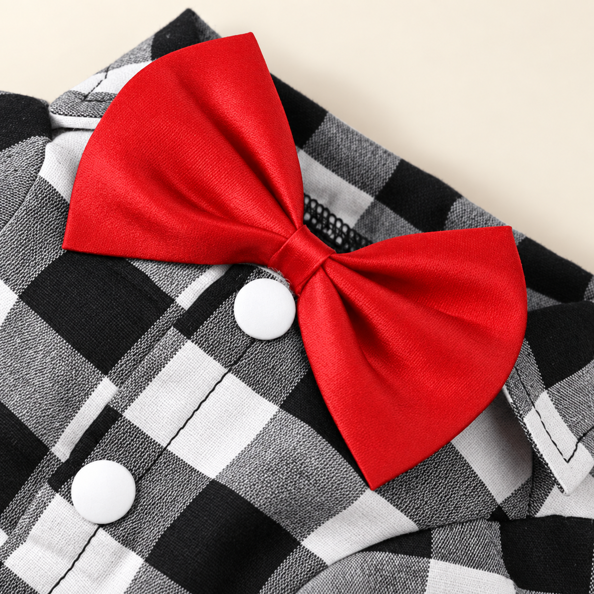 A bright red satin bow tie pinned to a black, white, and gray buffalo plaid shirt with white buttons, set against a light beige background.