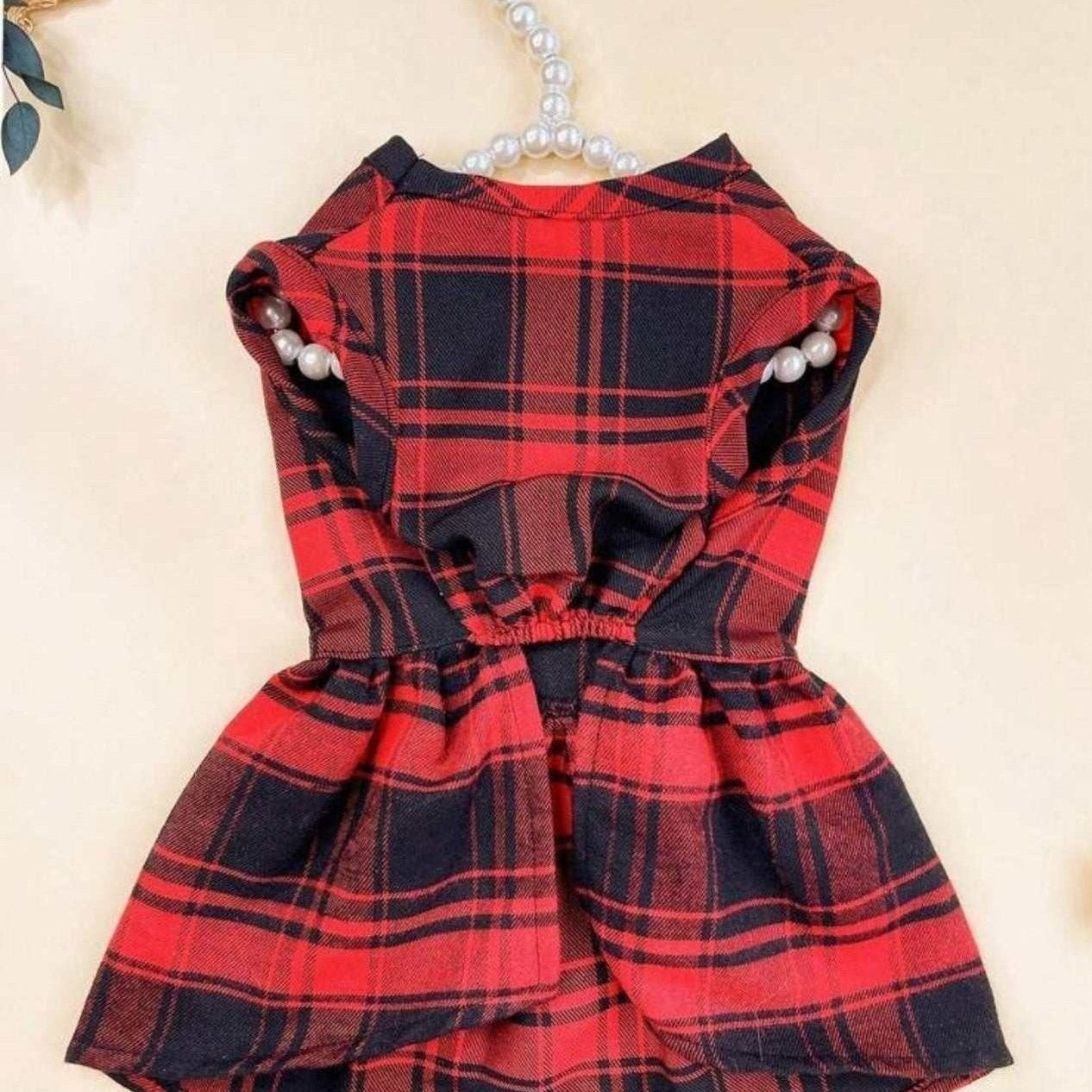 Close-up of red plaid dog dress showing festive tartan fabric detail and black bow accent