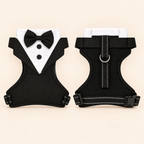 A pet harness shown from both front and back views, styled like a tuxedo with a black bow tie, white shirt, and black vest, on a light beige background.