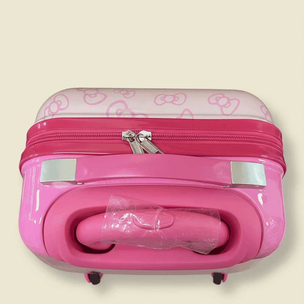 Side view of Hello Kitty pink suitcase with telescoping handle and reflective strips on cream background