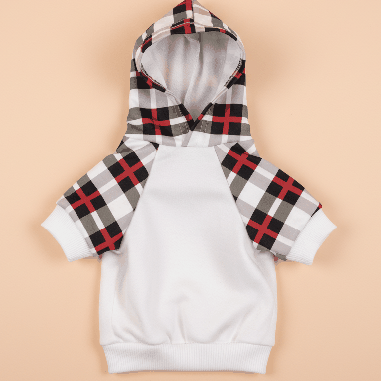 White dog hoodie with red black plaid sleeves on soft peach pastel background